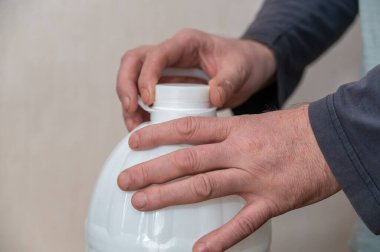 Bir adam beyaz bir şişe su açıyor. Adamın eli plastik şişenin mantarını tutuyor..