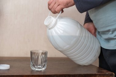 Bir adam bardağa su döker. Büyük, beyaz, plastik bir şişe taze su..