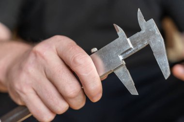 Kalibreyi tutan bir adamın eli. Nesnelerin dış ve iç boyutlarını ve derinliklerini ölçmek için yüksek hassasiyetli metal bir aleti olan yetişkin bir adam.