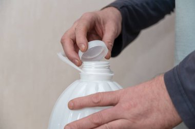 Bir adam beyaz bir şişe içme suyu açar. Adamın eli mantarı plastik şişenin üstünde tutuyor..