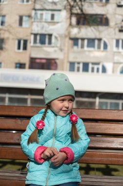 Parktaki bankta oturan bir kızın portresi. Ceketli ve şapkalı bir çocuk kameranın arkasına bakıyor. Gündüz vakti. İlkbahar.