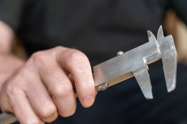 Kalibreyi tutan bir adamın eli. Nesnelerin dış ve iç boyutlarını ve derinliklerini ölçmek için yüksek hassasiyetli metal bir aleti olan yetişkin bir adam.