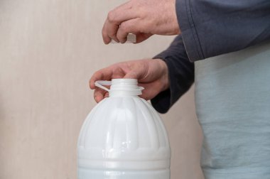 Bir adam beyaz bir şişe içme suyu açar. Adamın eli mantarı plastik şişenin üstünde tutuyor..