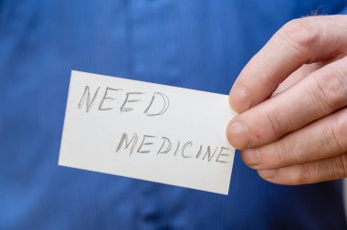 İlaç lazım. El yazısıyla yazılmış beyaz bir kağıt dikdörtgen tutan adam. Olgun bir adamın elinin yakın çekimi..