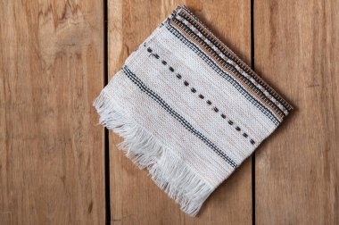 A white kitchen towel lies on the countertop of a wooden table. The fringed towel is fringed and patterned on the rough boards. Top view. Copy space