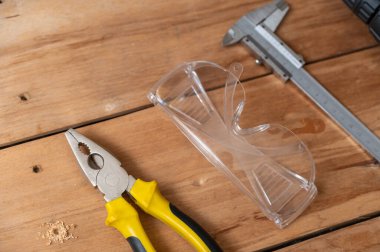 Caliper, pense ve güvenlik gözlükleri tahta bir yüzeyde bulunur. El ve ölçü aletleri. İş güvenliği, PPE konsepti. Seçici odak.