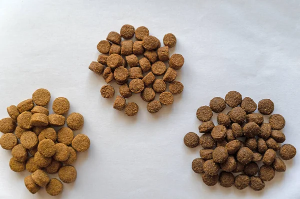 Three piles of different types of pet food against a neutral background. Round brown pellets of dry dog or cat food. Pet food. Top view.