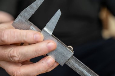 Kalibreyi tutan bir adamın eli. Nesnelerin dış ve iç boyutlarını ve derinliklerini ölçmek için yüksek hassasiyetli metal bir aleti olan yetişkin bir adam.