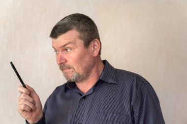 Elinde kalemle el kol hareketi yapan yetişkin bir adamın portresi. Kısa saçlı ve kır saçlı bir adam. Başka tarafa bakıyor. Kapalı.