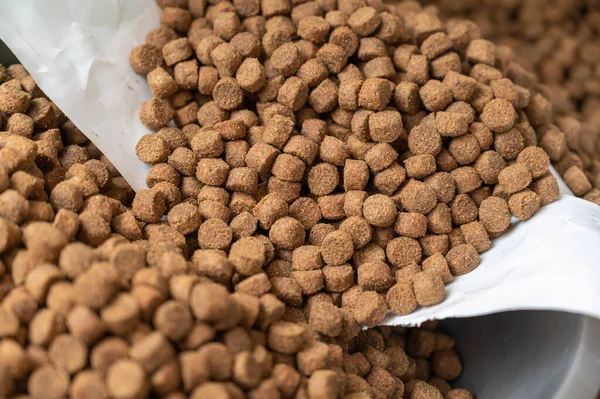 Close-up of dry pelleted pet food. Brown round pellets inside an open white bag. Pet food.
