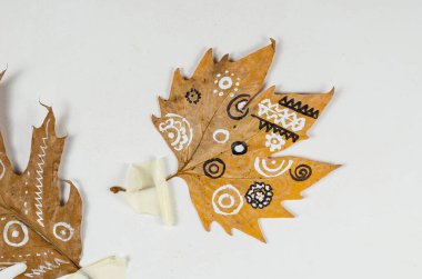 Süslü kuru yapraklar duvara koli bandıyla tutturulmuş. Etnik desenli sarı yapraklar. İçeride. Çağdaş sanat. Seçici odak.