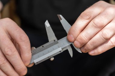 Kalibreyi tutan bir adamın eli. Nesnelerin dış ve iç boyutlarını ve derinliklerini ölçmek için yüksek hassasiyetli metal bir aleti olan yetişkin bir adam.