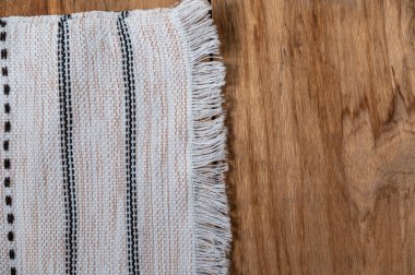 Ahşap bir masanın üstünde beyaz bir mutfak havlusu yatıyor. Fırfırlı havlu pürüzlü tahtalarda püsküllü ve desenli. Üst Manzara. Boşluğu kopyala