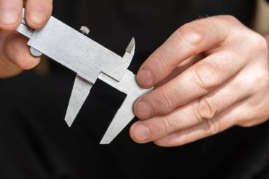 Kalibreyi tutan bir adamın eli. Nesnelerin dış ve iç boyutlarını ve derinliklerini ölçmek için yüksek hassasiyetli metal bir aleti olan yetişkin bir adam.