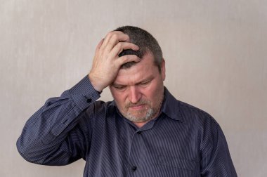 Aşağıya bakan sinirli bir yetişkinin portresi. Mavi çizgili gömlekli adam elini başına koydu. Kısa kahverengi saçlı, gri..