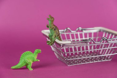 Mor arka planda dinozorlar ve alışveriş arabası. Dinozorlar boş alışveriş arabasının yanında. Yırtıcı hayvanların yeşil plastik minyatürleri. Seçici odak.