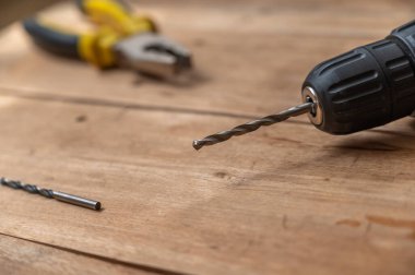 Elektrikli matkap ucu ve kerpeten tahta yüzeye dayanır. Elde taşınabilen elektrikli alet tahtaların üstünde. Seçici odaklanma. Kimse yok..