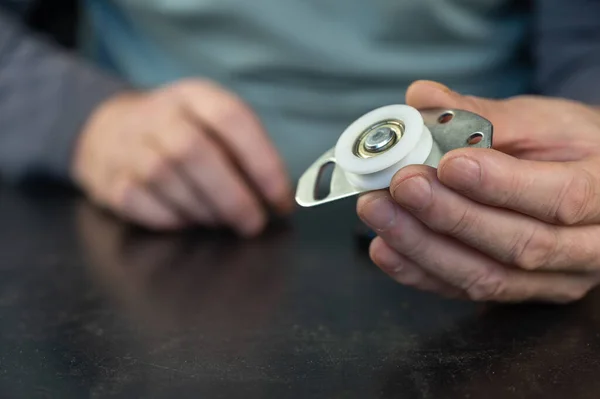 A grown man holds in his lower roller for a sliding door. Metal mounting plate with white plastic roller. Furniture hardware. Close-up. Selective focus.