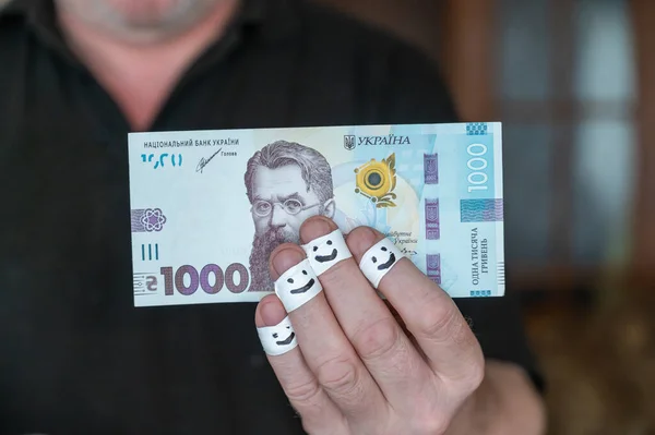 一个成年人手里拿着钱 一千乌克兰格里夫尼亚 他手指的第一个指节用白色丝带包裹着 绷带上涂着笑脸 — 图库照片