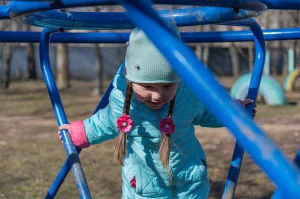 Çocuk parkında oynayan bir kız. Çocuk salıncağının metal yapısının içinde beş yaşında bir çocuk. Saçları örgülü, uzun saçlı bir kız. İlkbahar. Seçici odak.
