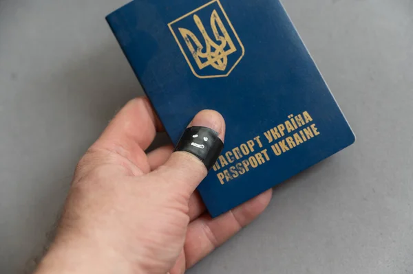中年の男性は灰色の背景に対して彼の手にウクライナのパスポートを保持しています 親指のファランクスが黒い電気テープで包まれている 幸せな笑顔がテープに描かれています — ストック写真