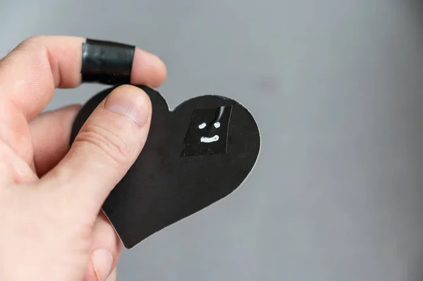 A man holding a black heart in his hand. Smiling face drawn in white marker on paper heart. The hand of a middle-aged man. Positive eosion, love, happiness concept. Close-up. Selective focus.