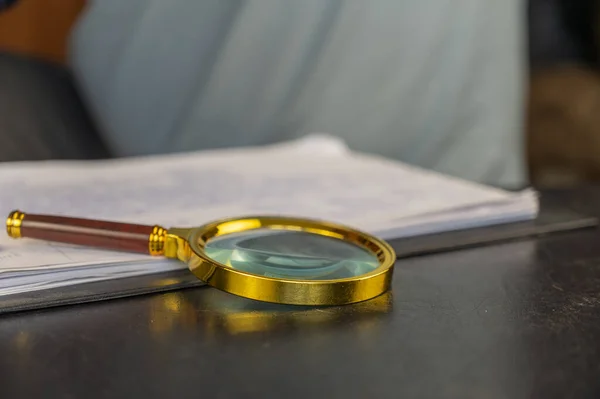 A magnifying glass in a gold frame lies on a black table. Selective focus.