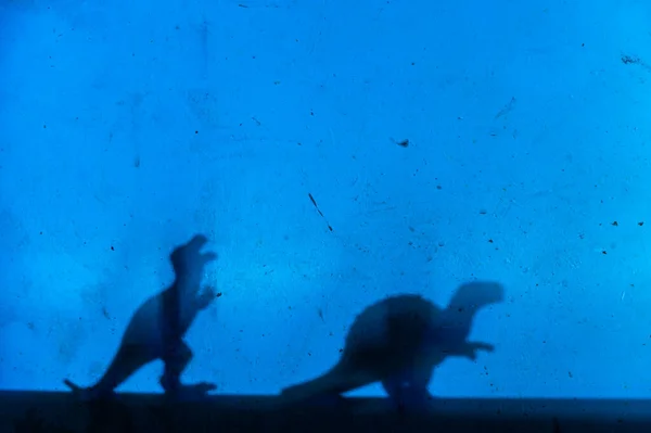 青い壁に黒い恐竜のシルエット プレデターと草食動物 小さなミニチュアで創造的な背景 選択的フォーカス スペースのコピー — ストック写真