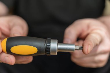 Tornavida tutan olgun bir adamın eli. Değiştirilebilir bitlerle el aracı.