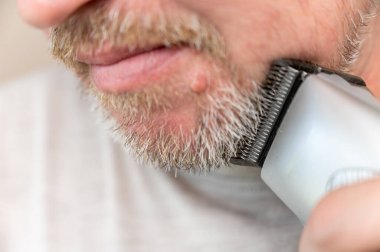 Olgun bir adamın tıraş olurken odaklanmamış bir fotoğrafı. Bir adamın yüzünün alt kısmı. Adam saç makasıyla sakal kesiyor. Sakallı adam. Sakallı ve bıyıklı gri saçlı. Defocus, bulanık. Seçici odak.