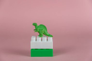 Çocuğun yapı taşlarının üzerinde duran dinozor minyatürü. Yırtıcı bir dinozorun arka ayaklarının üzerinde duran küçük yeşil minyatürü. Pembe arka plan. Seçici Odaklanma.