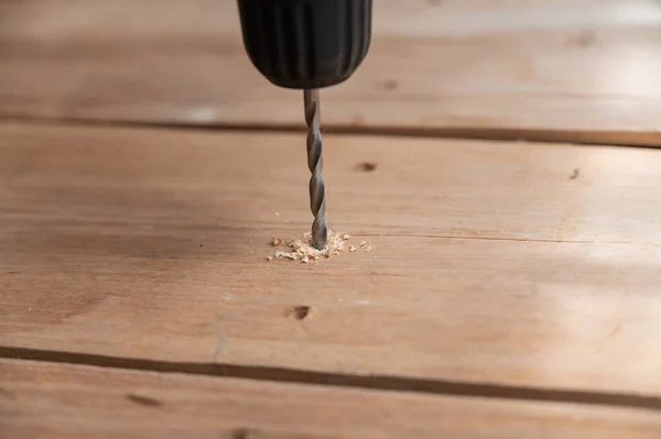 The process of drilling a wooden board with an electric drill. Hand-held power tool. Close-up. Selective focus. No people.