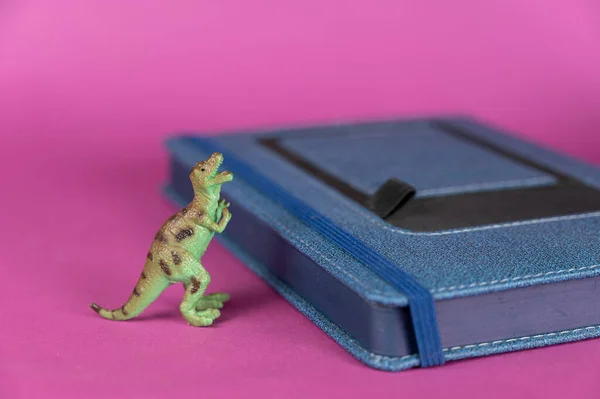 恐竜と紫の背景に青の日記を閉じた 獲物の動物の緑のプラスチック製のミニチュア 選択的焦点 — ストック写真