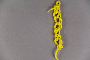Gri bir arka plana karşı sarı bir kordon. Yuvarlak dantel düğümlerle örülmüş. Yakın plan. Seçici odak.
