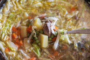 Bir kaşık dolusu yemek. Lezzetli bir lahana, patates, soğan, havuç, yeşil bezelye, tavuk ciğeri, tuz ve baharat çorbası. Yakın çekim görüntüsü. Seçici odaklanma. Birinci şahıs görünümü