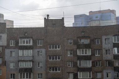 Yüksek binanın önünde yoğun sağanak yağmur duvarı var. Yaz yağmurunun dokusu. Apartmanın tuğla binası. Yoğun bulut örtüsü. Bulanık hareket. Seçici odaklanma. Gürültü, tahıl etkisi
