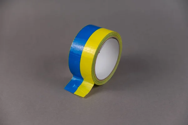 Yellow and blue duct tape. Reel of colored duct tape against the gray background. Selective focus. No people.