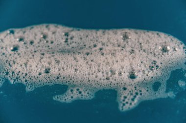 Renkli arka planda sabun köpüğü. Mavi yüzeyde beyaz deterjan köpüğü kabarcıkları. Şampuan köpüğü dokusu. Seçici odak.