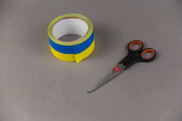 Yellow and blue duct tape and scissors. Reel of colored duct tape against the gray background. Selective focus. No people.
