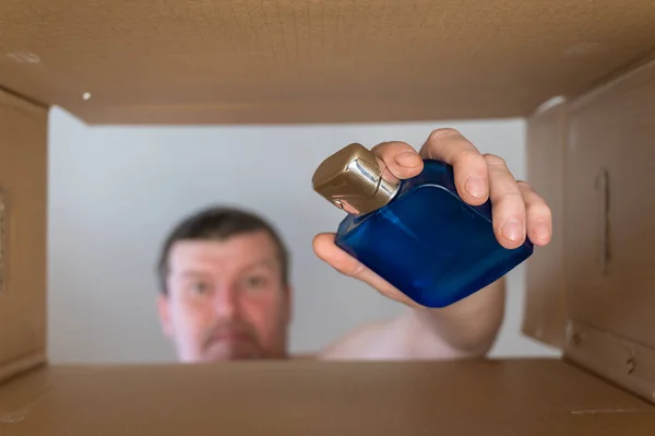 A man pulls perfume out of a cardboard moving box. Blue glass bottle of perfume with a silver cap. Bottom view. Inside view. Close-up. Selective focus.