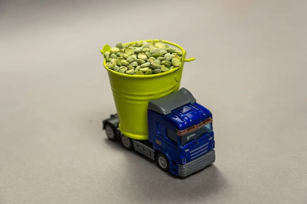 Transportation of agricultural products concept. A truck is carrying dry split peas in a small bucket. Green bucket stands on top of a child\'s toy car. Green beans. Close-up. Selective focus.