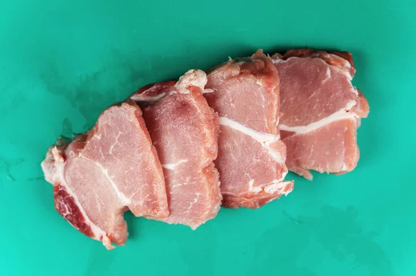 Raw pork is cut crosswise into portioned pieces. Four portioned pieces of pork shoulder. Raw meat lies on a green wet surface. Food, ingredients. Selective Focus