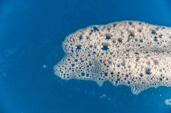 Soap foam against a colored background. Bubbles of white detergent foam on the blue surface. Shampoo foam texture. Selective focus.