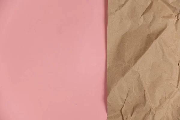Wrapping paper against a pink background. Crumpled sheet of light brown paper lies on colored surface. Top view. Copy space for text and design elements.