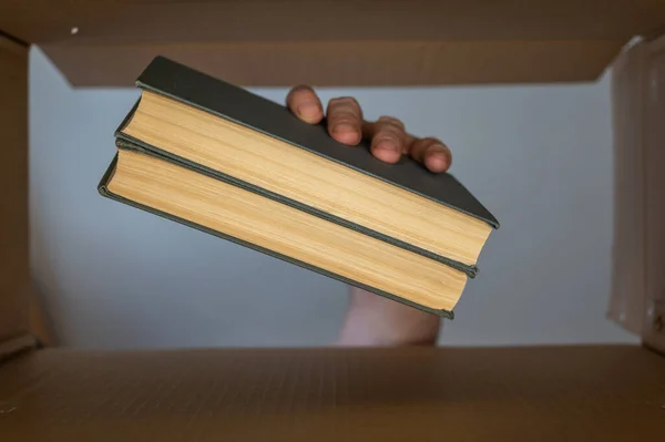 Hand Van Een Man Stopt Twee Boeken Een Kartonnen Doos — Stockfoto