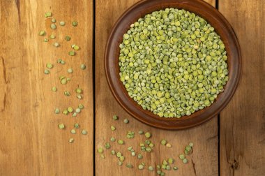 Kuru bezelye. Kahverengi kil kase. Ahşap bir arka plana yeşil bezelye serpilmesi. Pişmemiş yemek. Sağlıklı yiyecekler. Yakın plan. Seçici odaklanma. Metin ve tasarım ögeleri için boşluk kopyala.