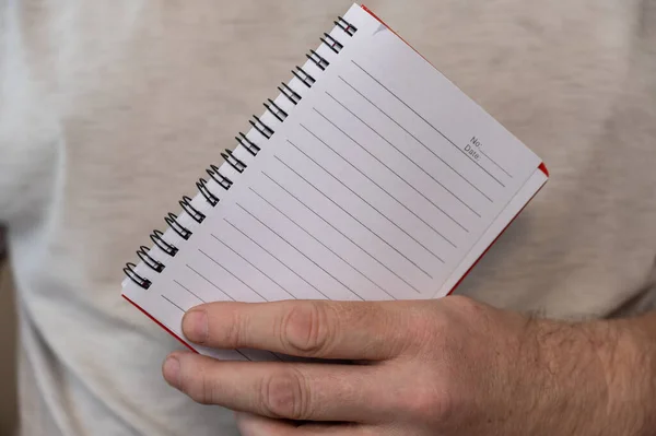 A middle-aged man is holding an open notebook on a spring. The blank pages of the notebook are in a line. Notebook in a man\'s hand. Middle section of a mature man in a gray T-shirt. Selective Focus.