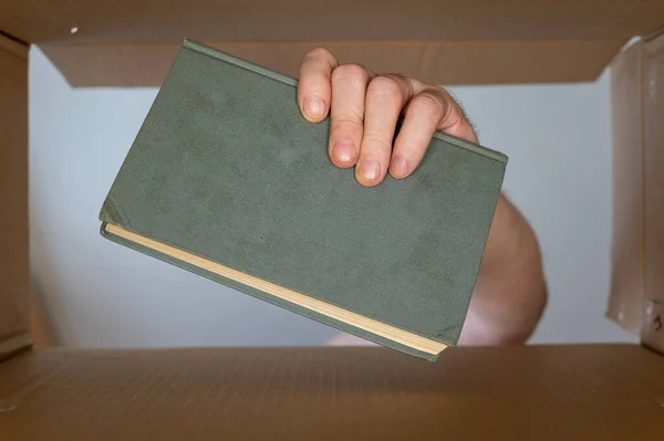一个人的手从一个纸板箱里掏出一本书 一本旧的绿色精装书 底部的观点 有选择的重点 — 图库照片