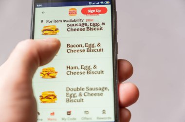 Adam telefonundan yemek sipariş ediyor. Erkek el menüde hamburgeri seçer. Burger King Corporation, dünya çapında fast food restoranları zinciri olan bir Amerikan şirketidir. Mykolaiv, Ukrayna - 06 27 2022