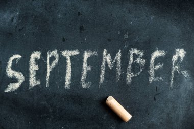 Eylül. Siyah karatahtaya sarı tebeşirle yazılmış ilk sonbahar ayının adı. El yazısıyla yazılmış bir metin. Yanında renkli bir tebeşir parçası var..